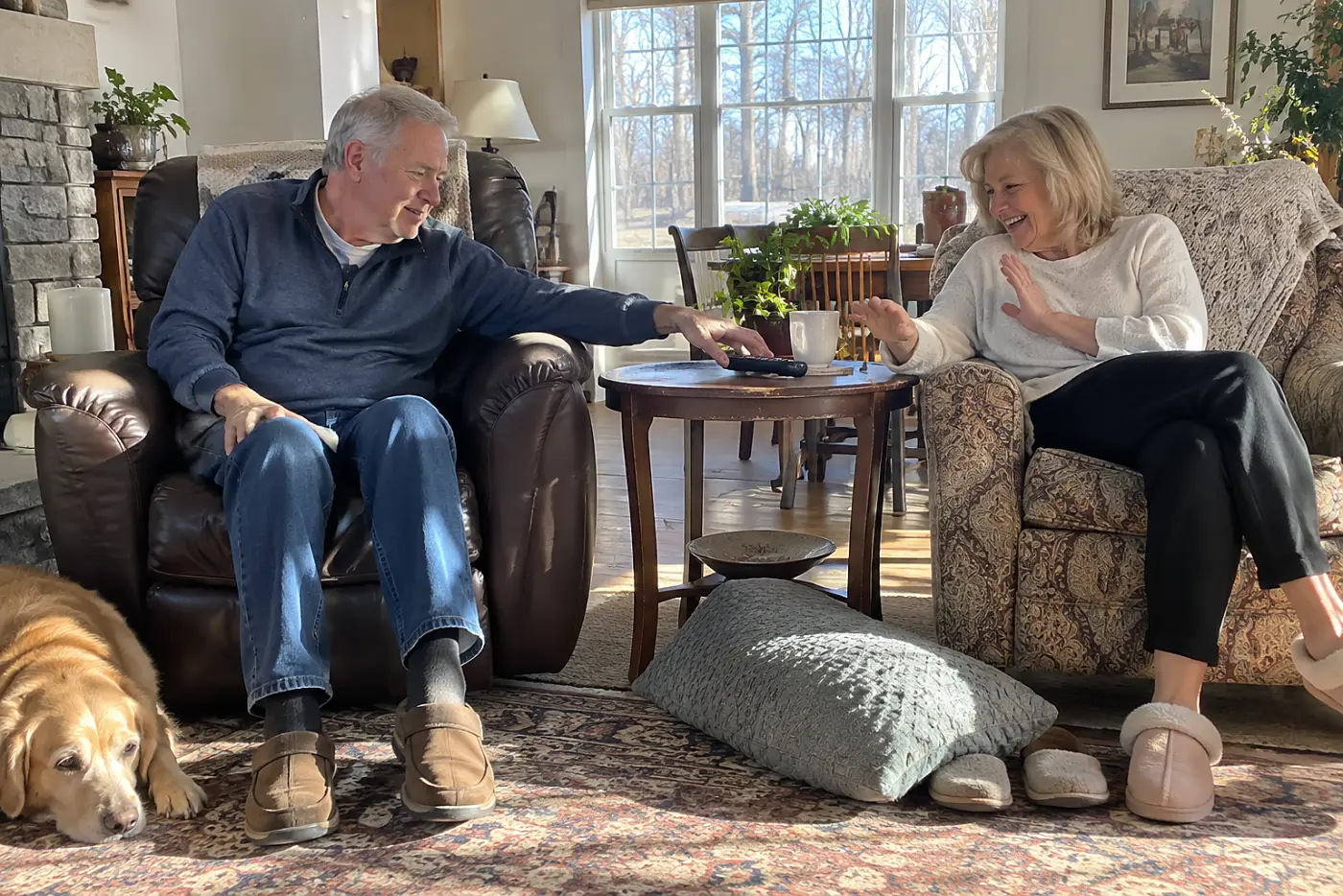 Older couple sitting in separate living room chairs with a remote between them.