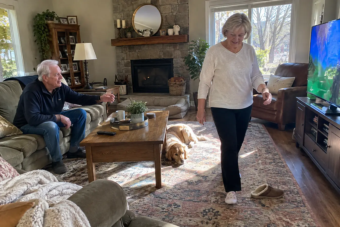 Older woman walking across her living room while the television is on.