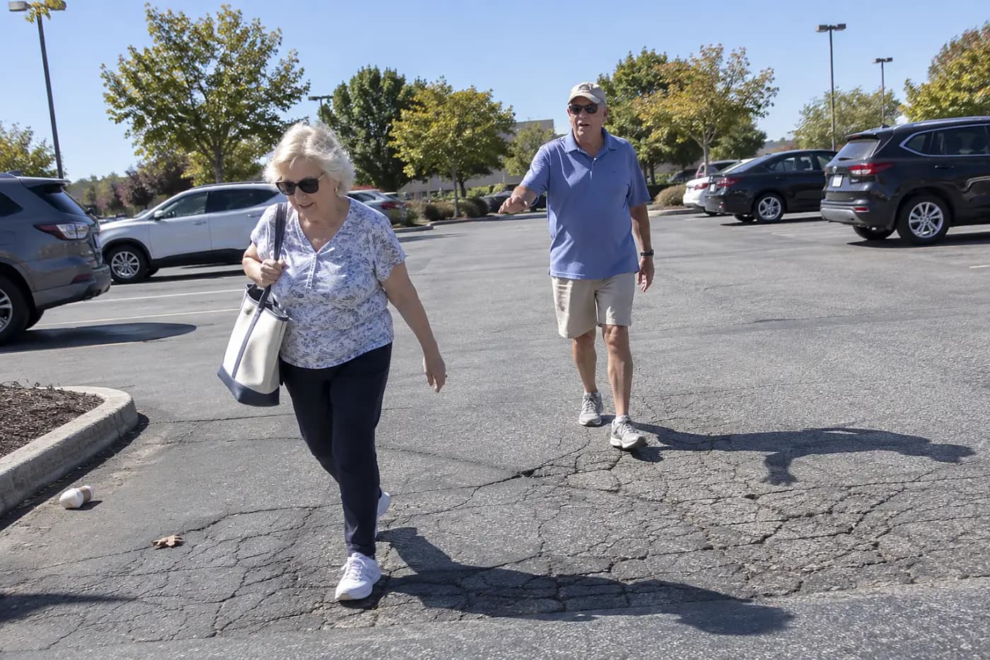 Older woman walking around a cracked section of a store parking lot.