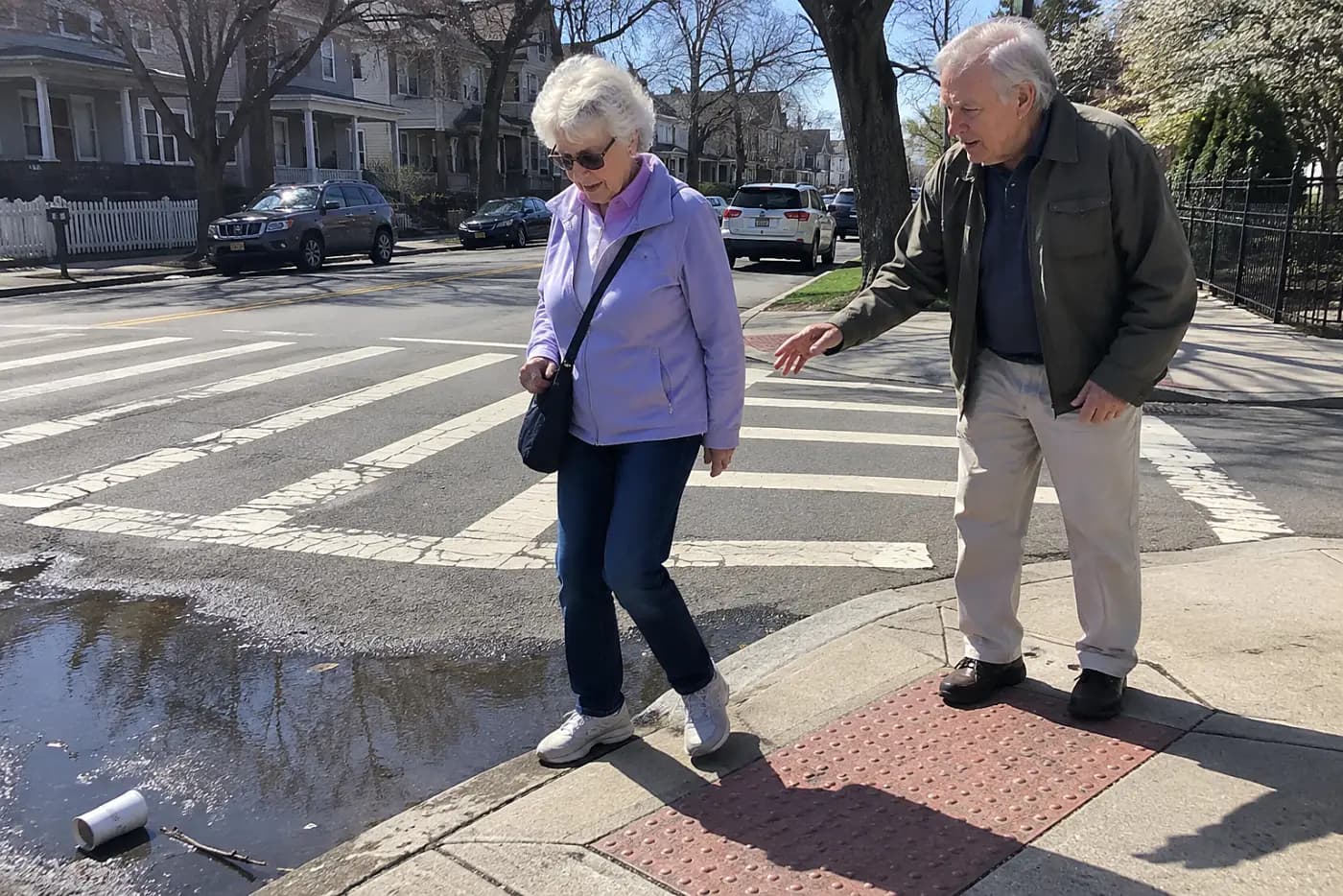 Older woman pausing at a curb cut beside a marked crosswalk.
