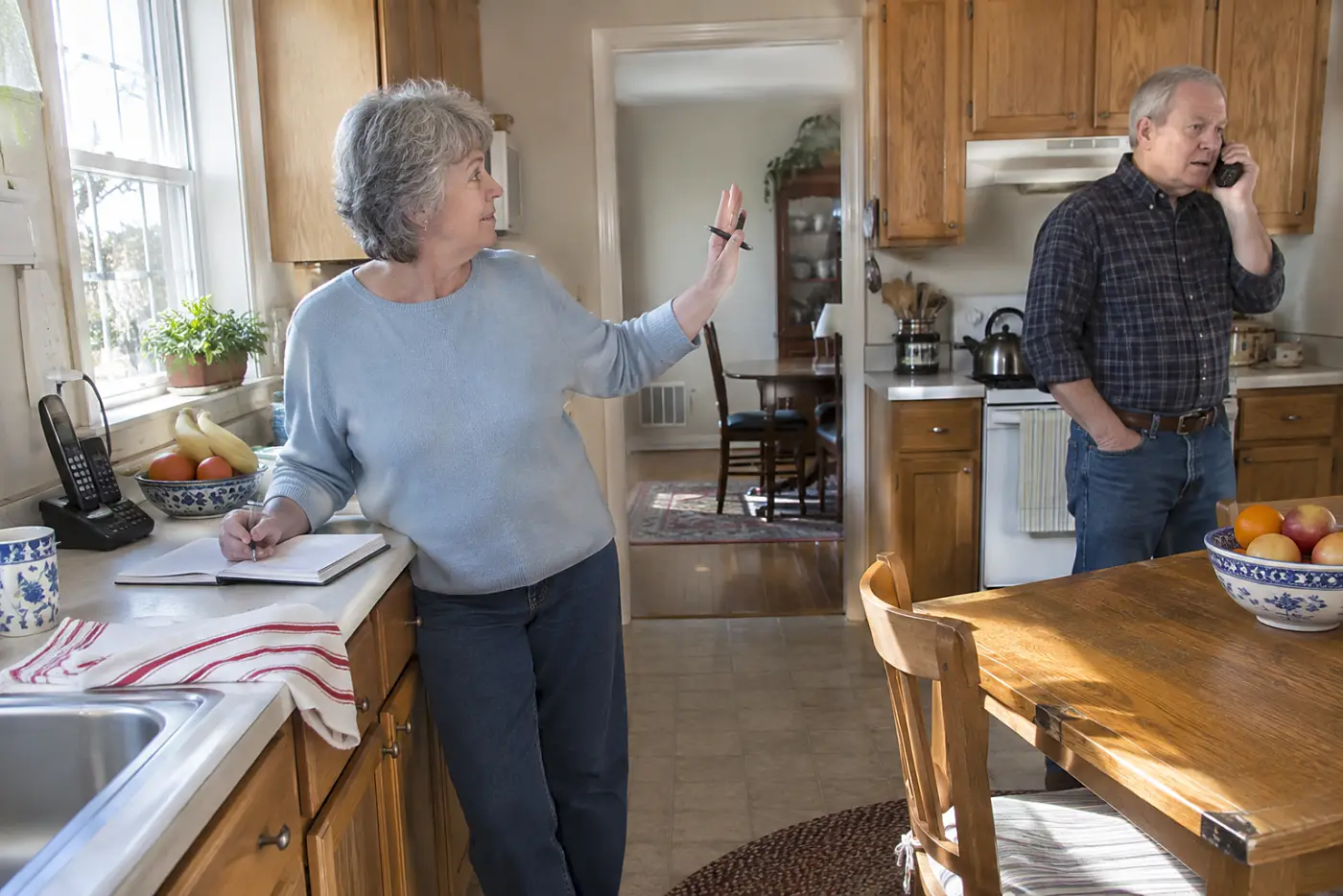 Older woman writing phone numbers in an address book beside her home phone.