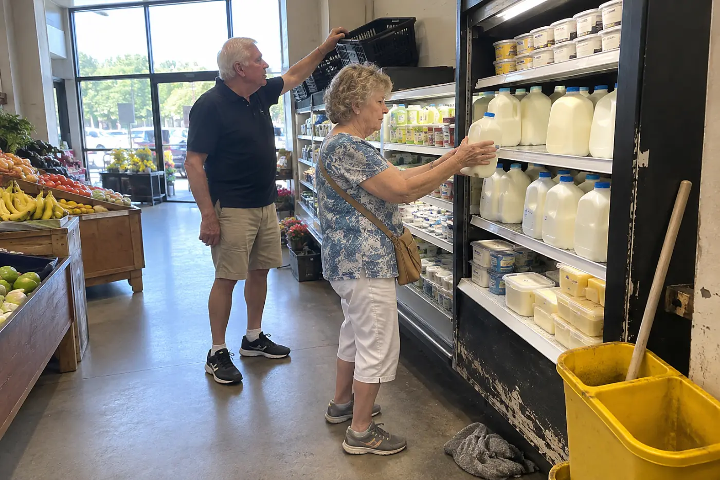 Older woman picking up a carton of milk in a grocery aisle.