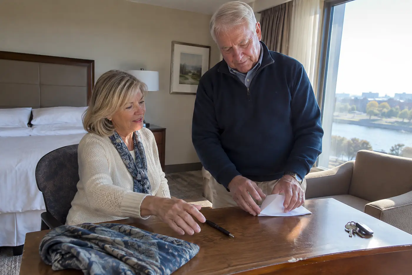 Older woman writing on a paper calendar at a hotel desk.