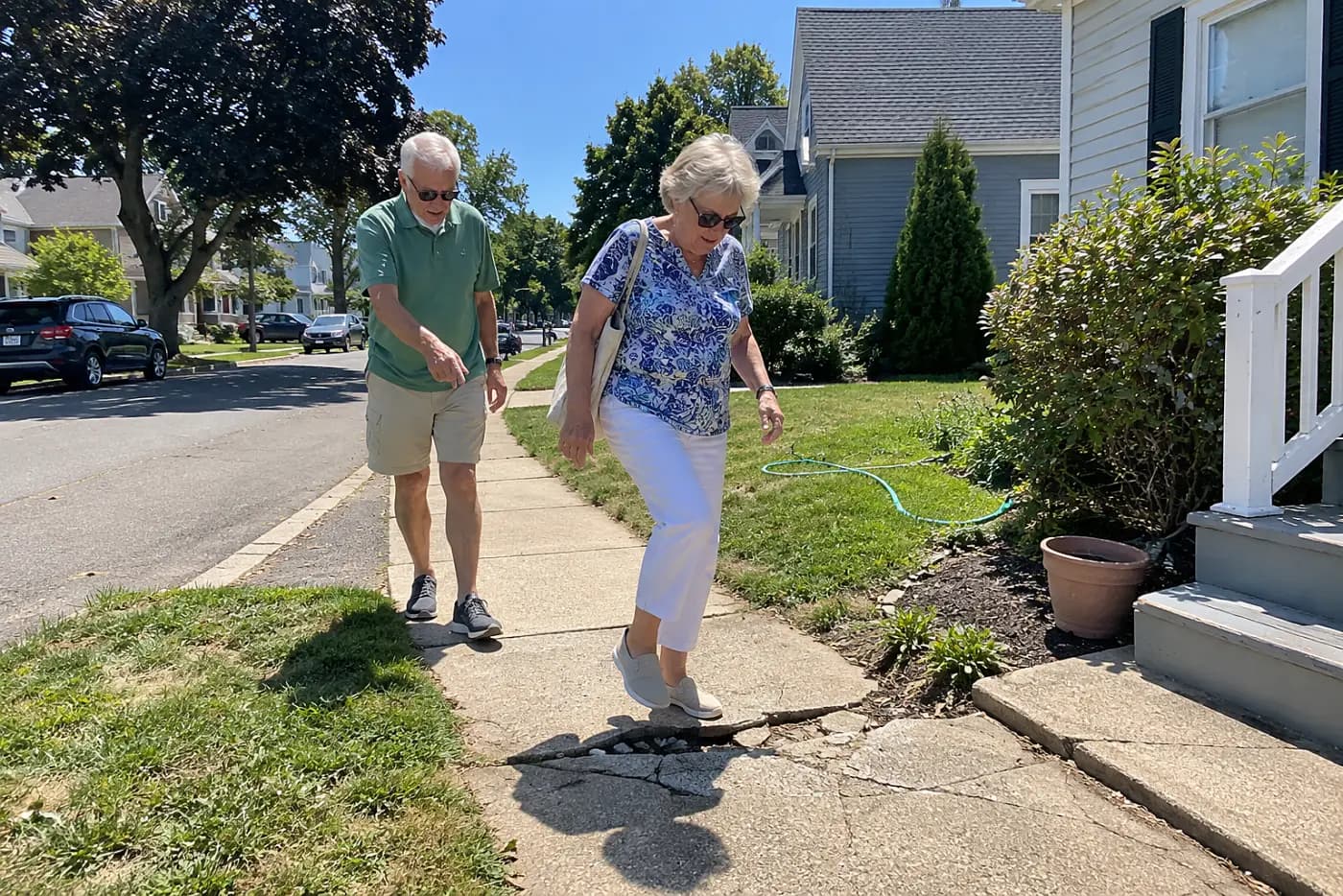 Older woman walking along a cracked sidewalk in a residential neighborhood.