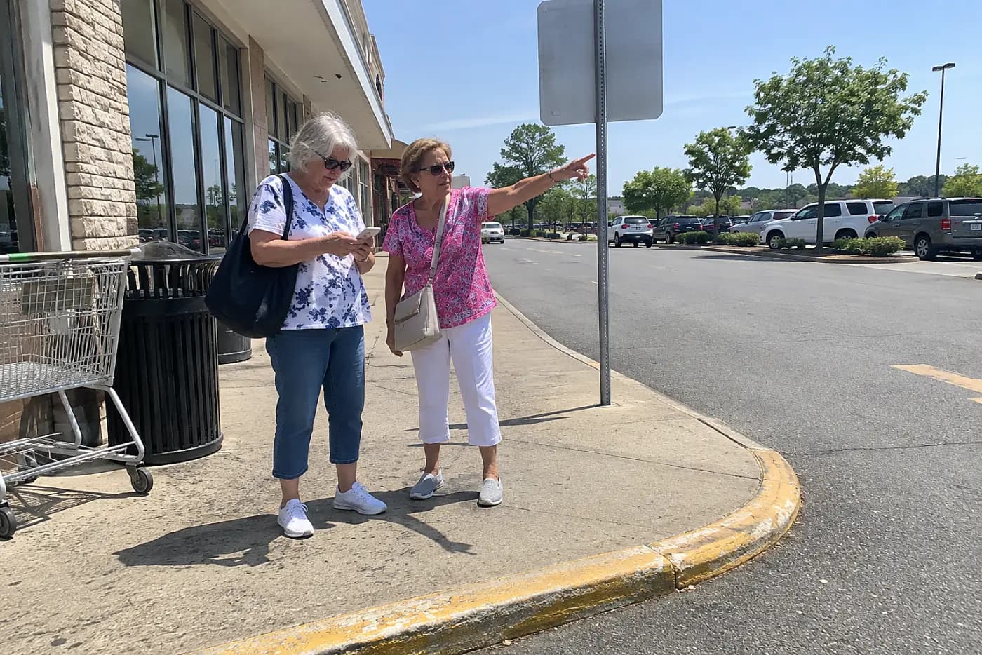 Older woman checking her phone beneath a highway exit sign near a row of stores.