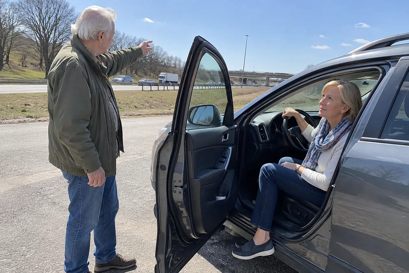 Older woman sitting in a parked car near a highway entrance.