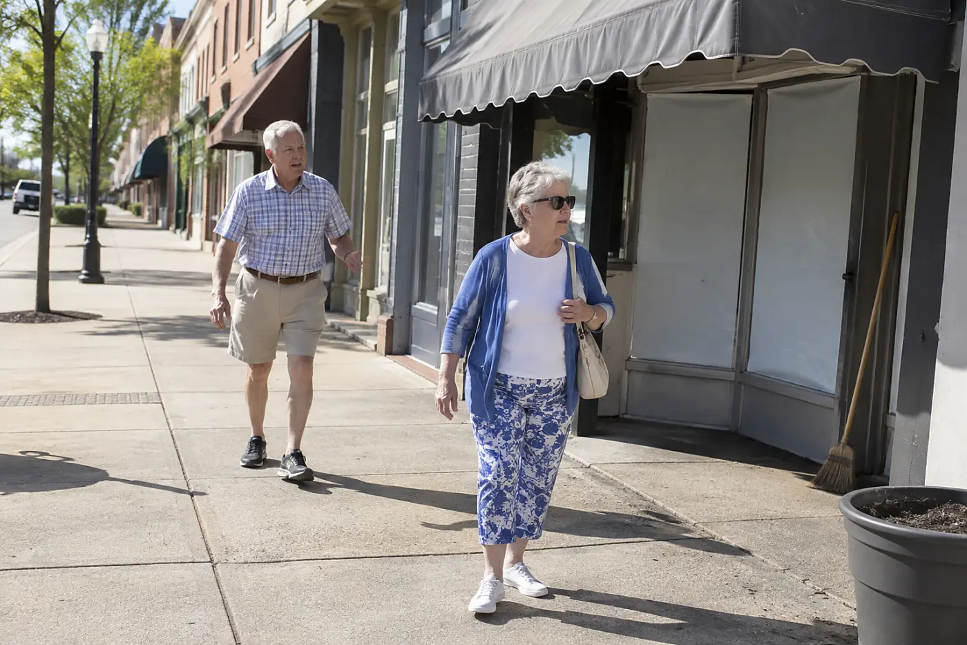 Older woman walking past closed storefronts on a well-lit main street.