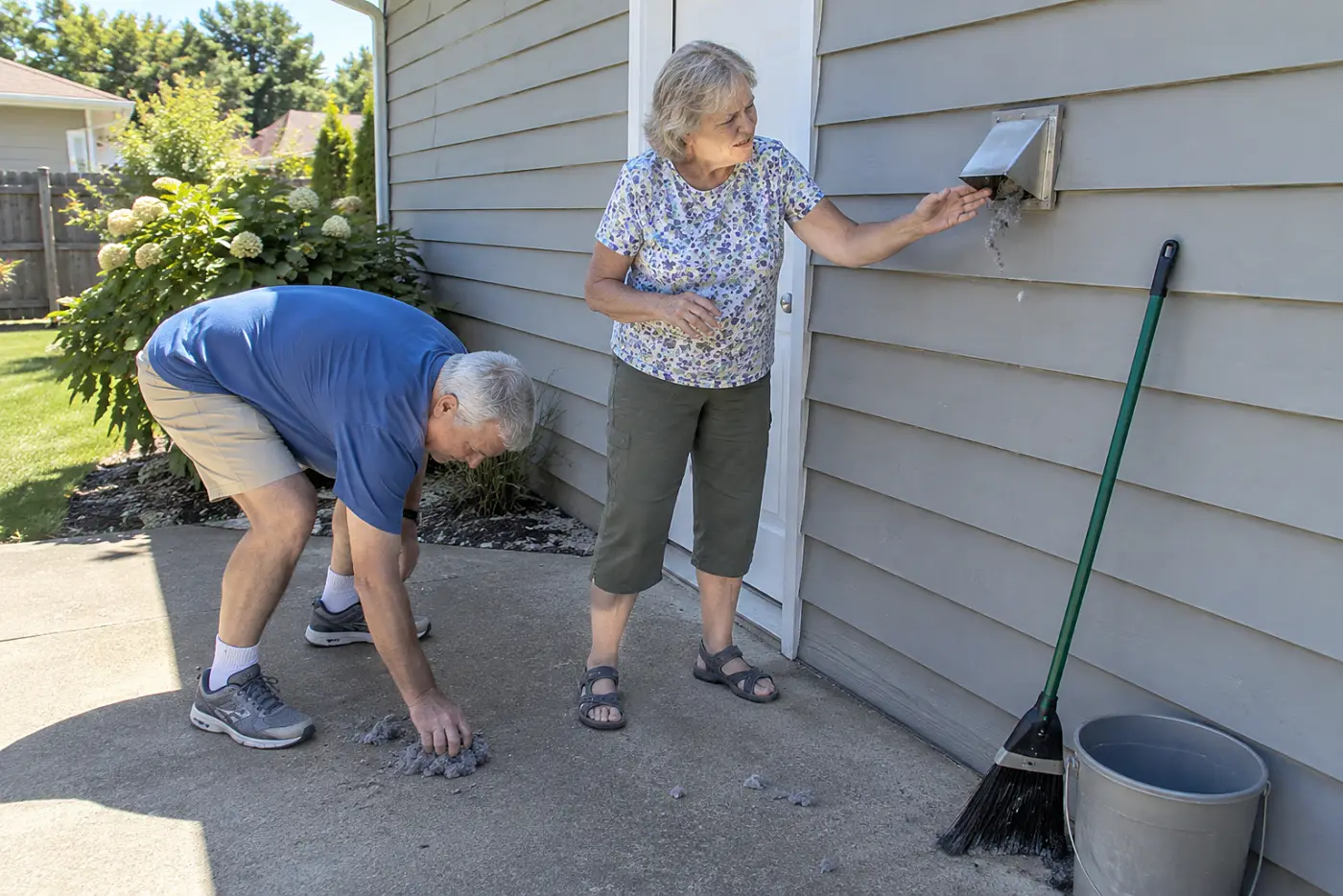 Older woman checking the dryer vent flap outside her laundry room.