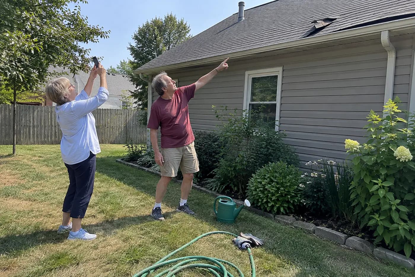 Older woman photographing worn roof shingles from her backyard.