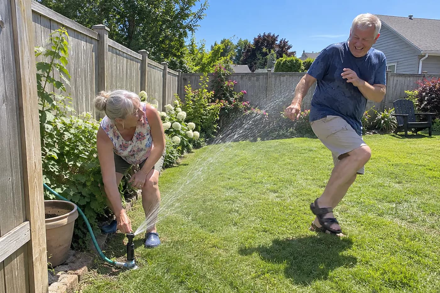 Woman adjusting a sprinkler head beside her fence.