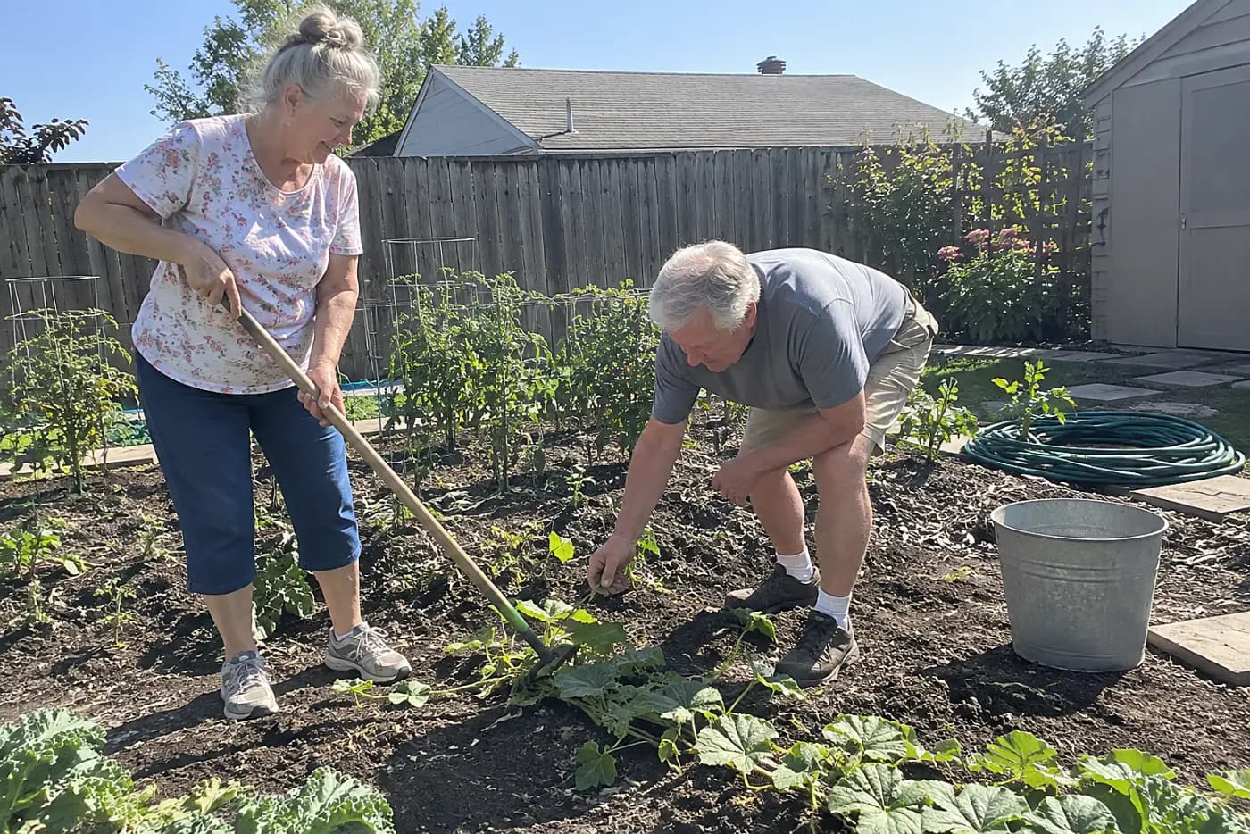 Older woman trying a long-handled cultivator in a small vegetable bed.