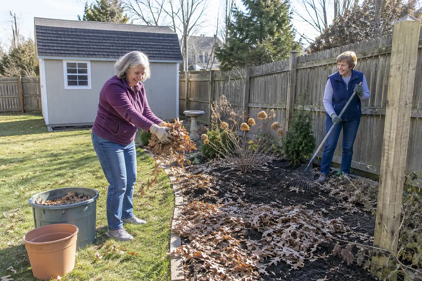 Older woman spreading clean leaves over bare soil in a backyard bed.