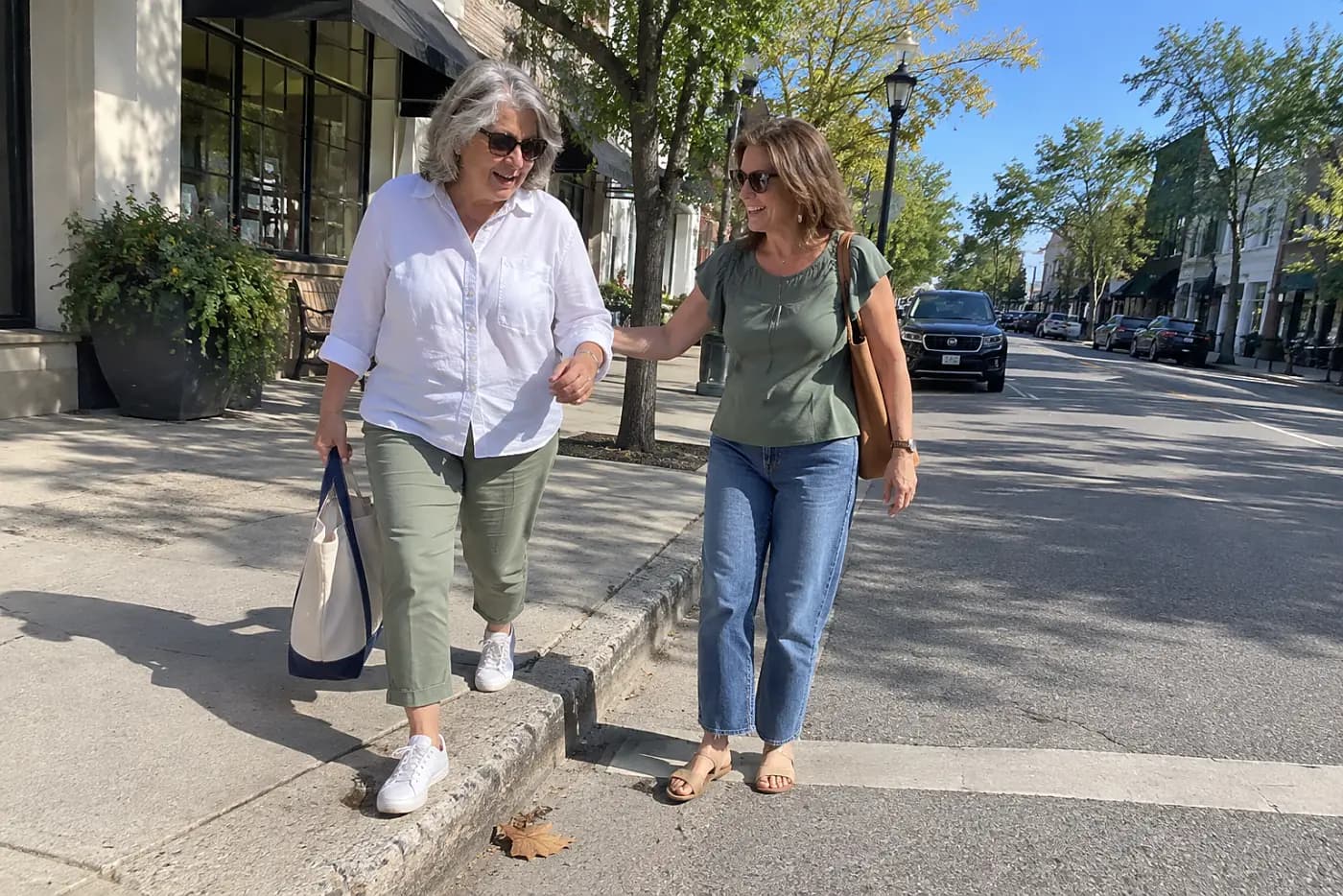 Older woman stepping off a curb while speaking to a person beside her.