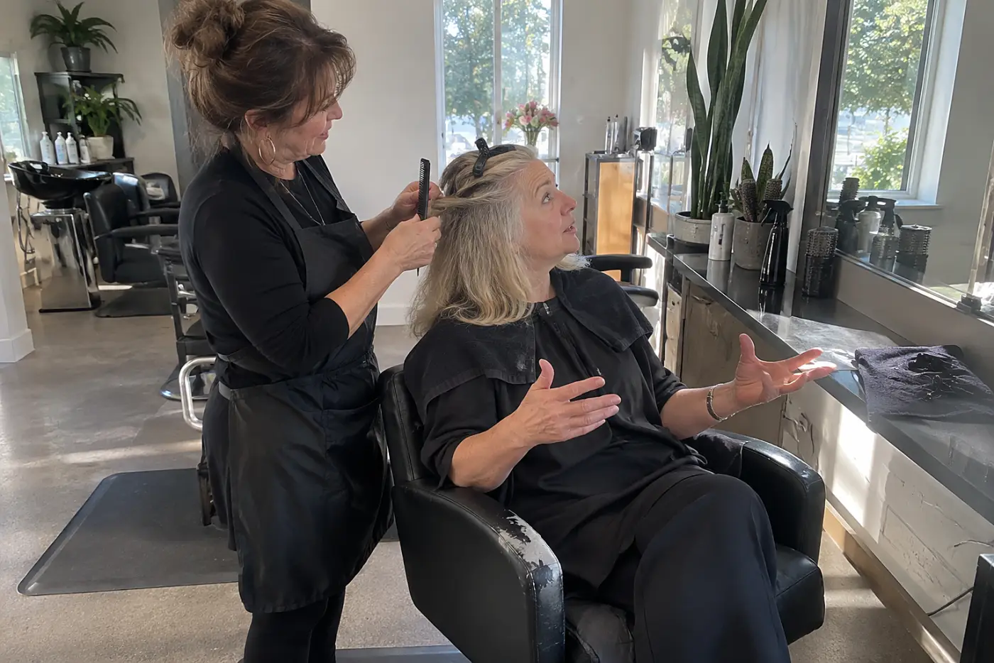 Older woman speaking with a colorist while seated before a salon mirror.