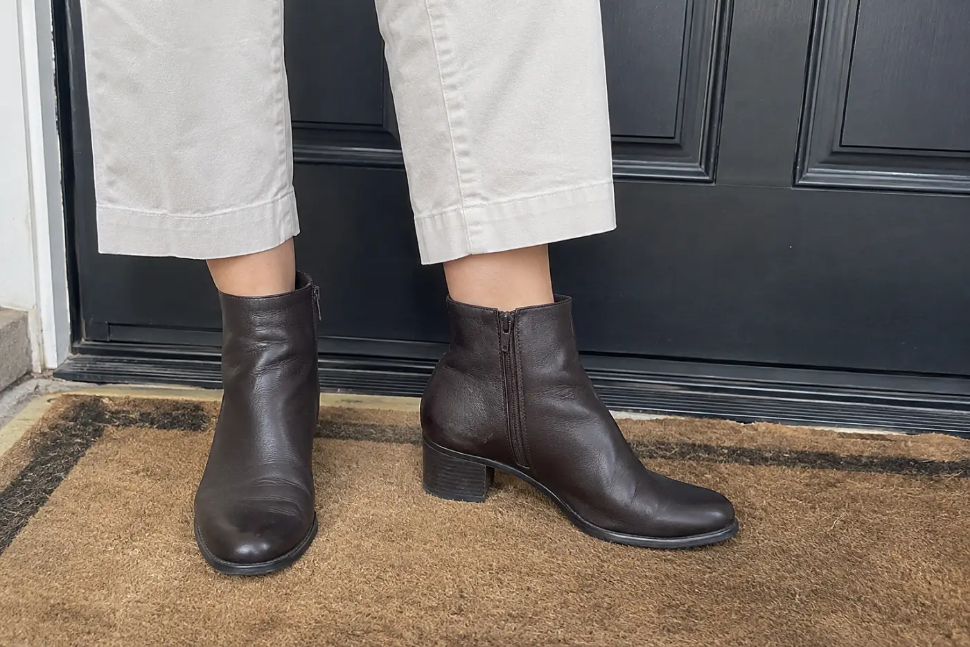 A low-heeled ankle boot is centered beneath cropped trousers on a woman over 50 standing by her front door.