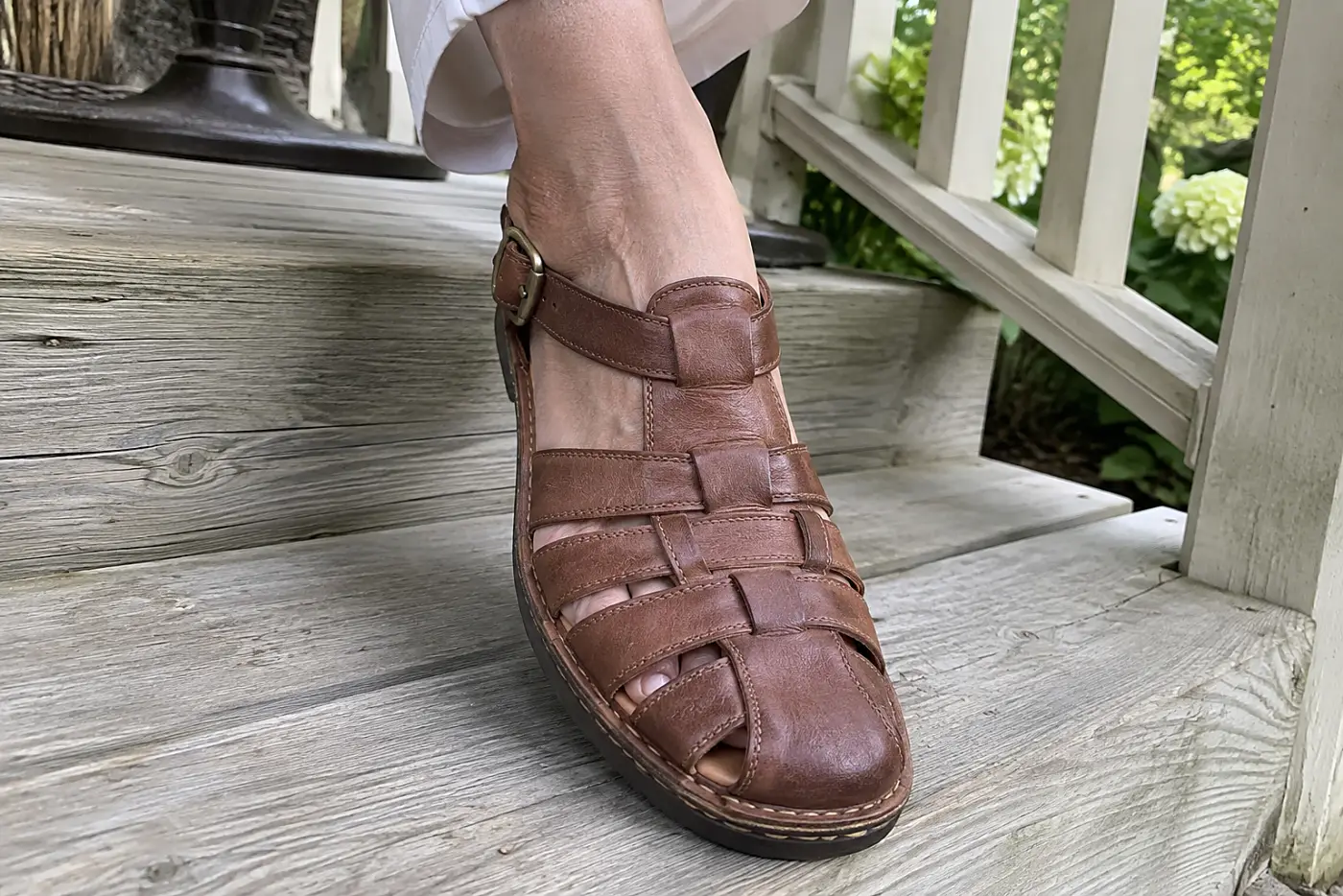 A fisherman sandal is centered on the foot of a woman in her sixties seated on a porch step.