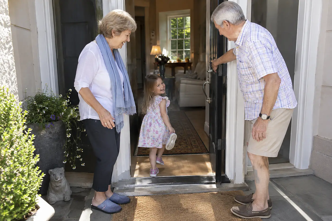 Older woman standing back as a child enters her front doorway.