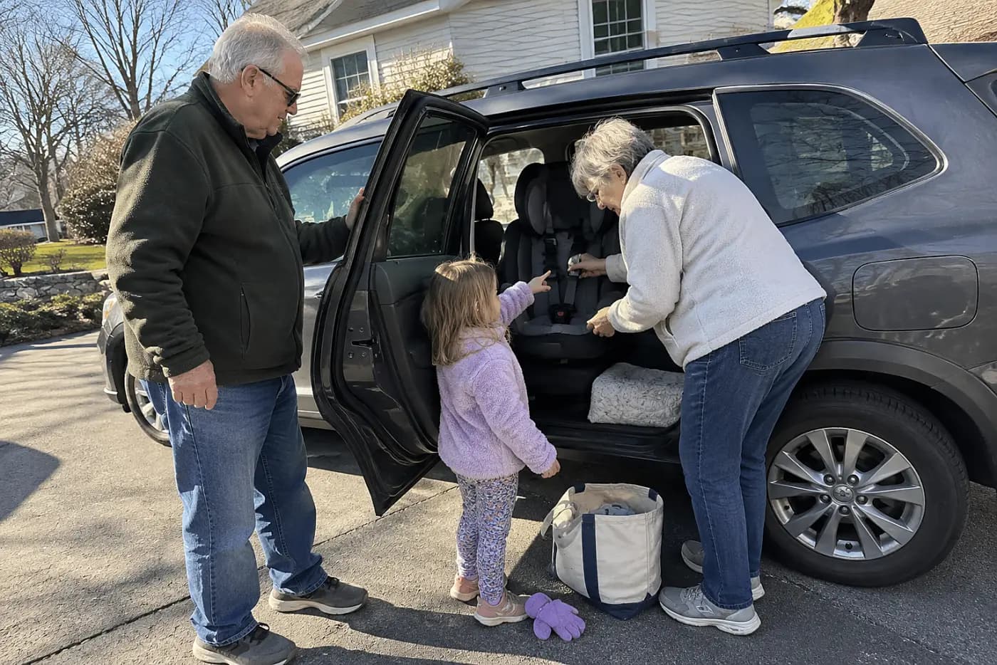 Older woman checking a child’s car seat in the back of a parked car.