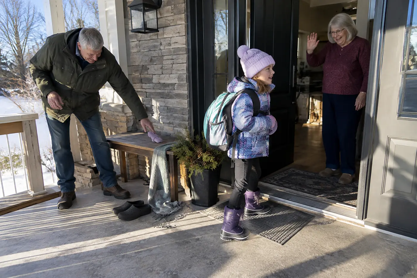 Older woman waving goodbye to a child at the front door.