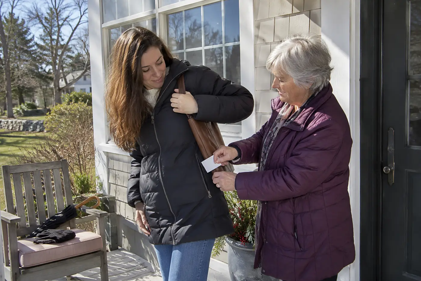 Grandmother tucking a contact card into her granddaughter’s zipped coat pocket.