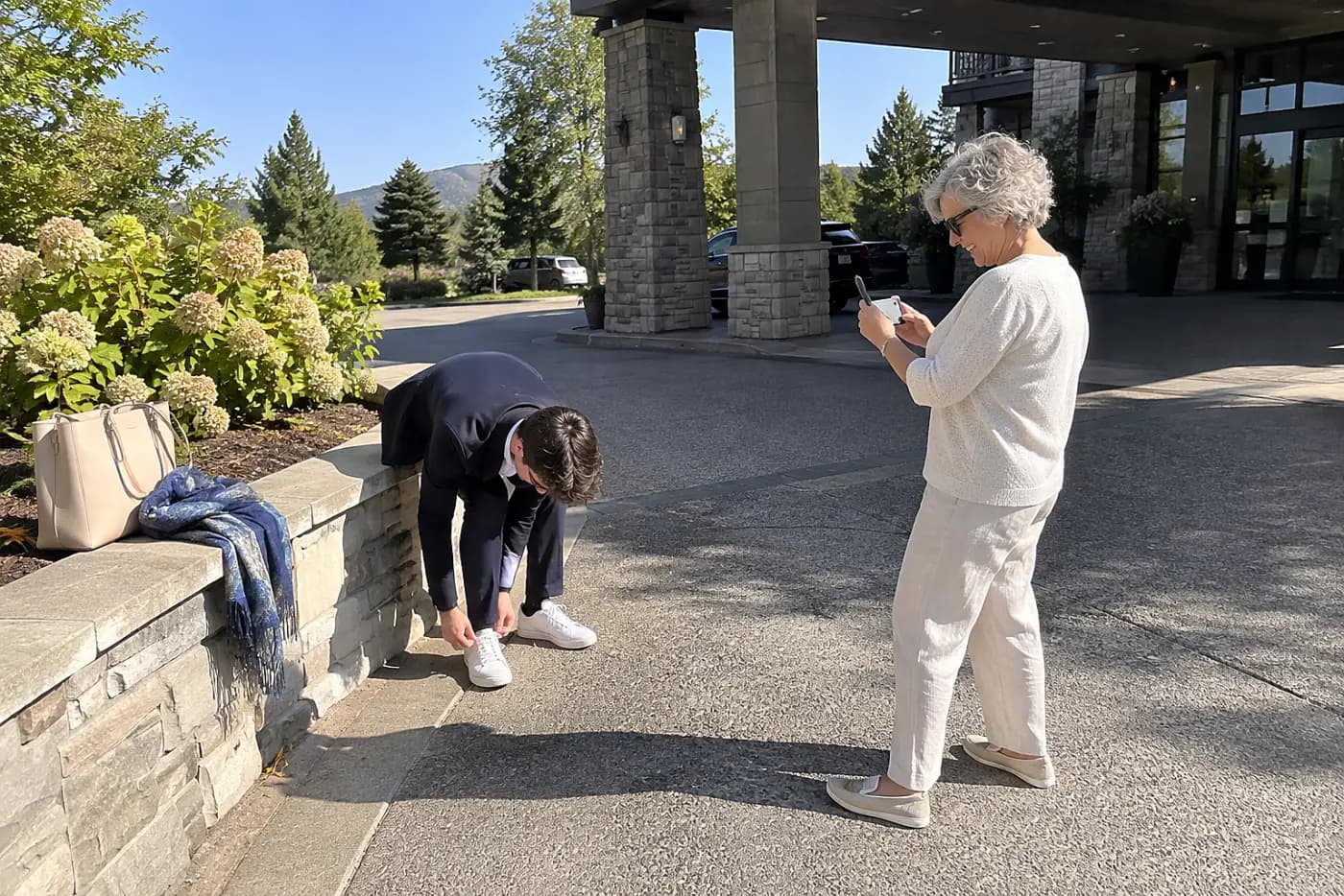 Grandmother photographing her grandson’s jacket and shoes outside a hotel.