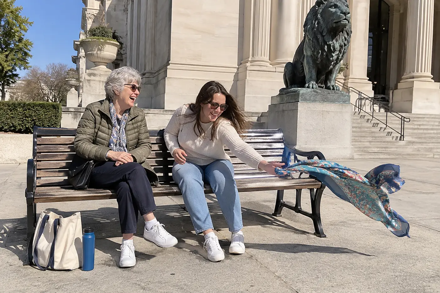 Grandmother and granddaughter sitting on a bench outside a museum entrance.