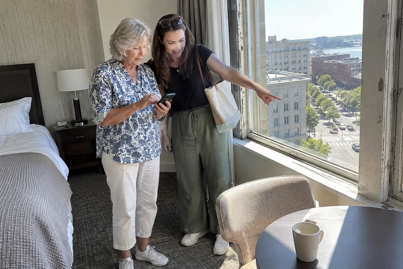 Grandmother tracing a walking route on her phone beside a hotel window.