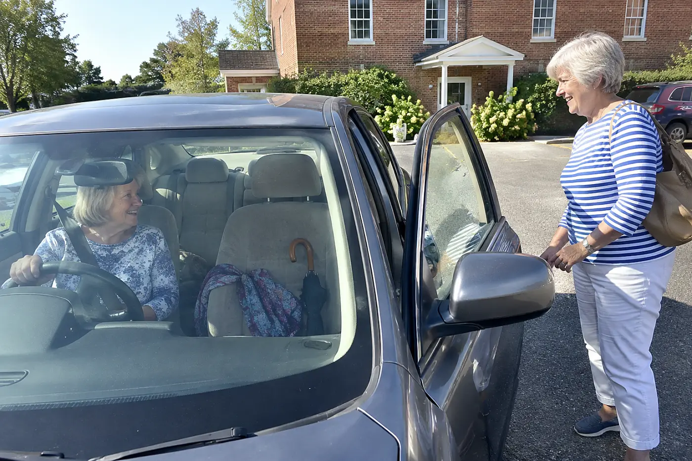 Older woman sitting in a parked car near a familiar building.