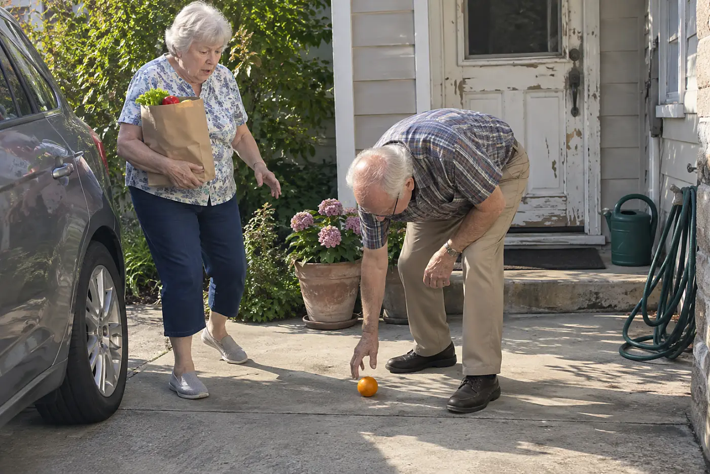 Older woman carrying a grocery bag from her car to her front door.