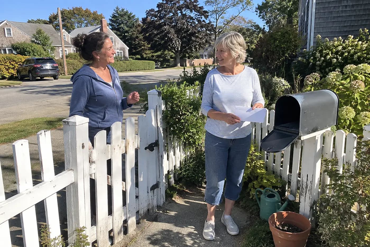 Older woman holding an unopened envelope beside her mailbox.