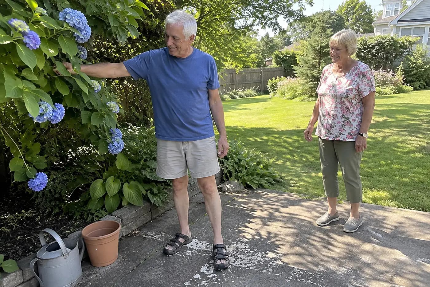 Older woman photographing a shaded flower bed from her patio.
