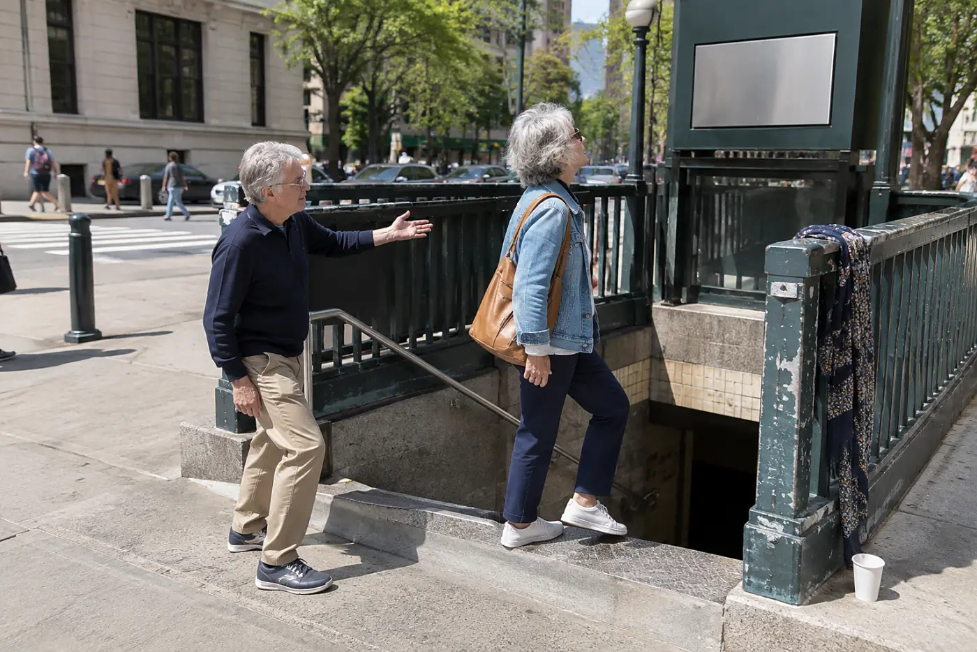 Older woman checking a station elevator sign beside a subway entrance.