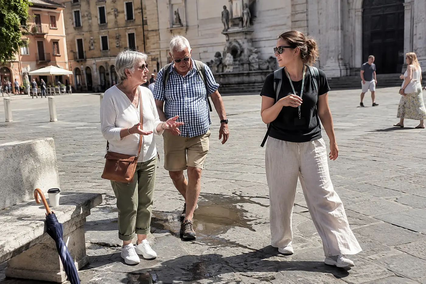 Older woman asking a tour guide a question beside a town square.