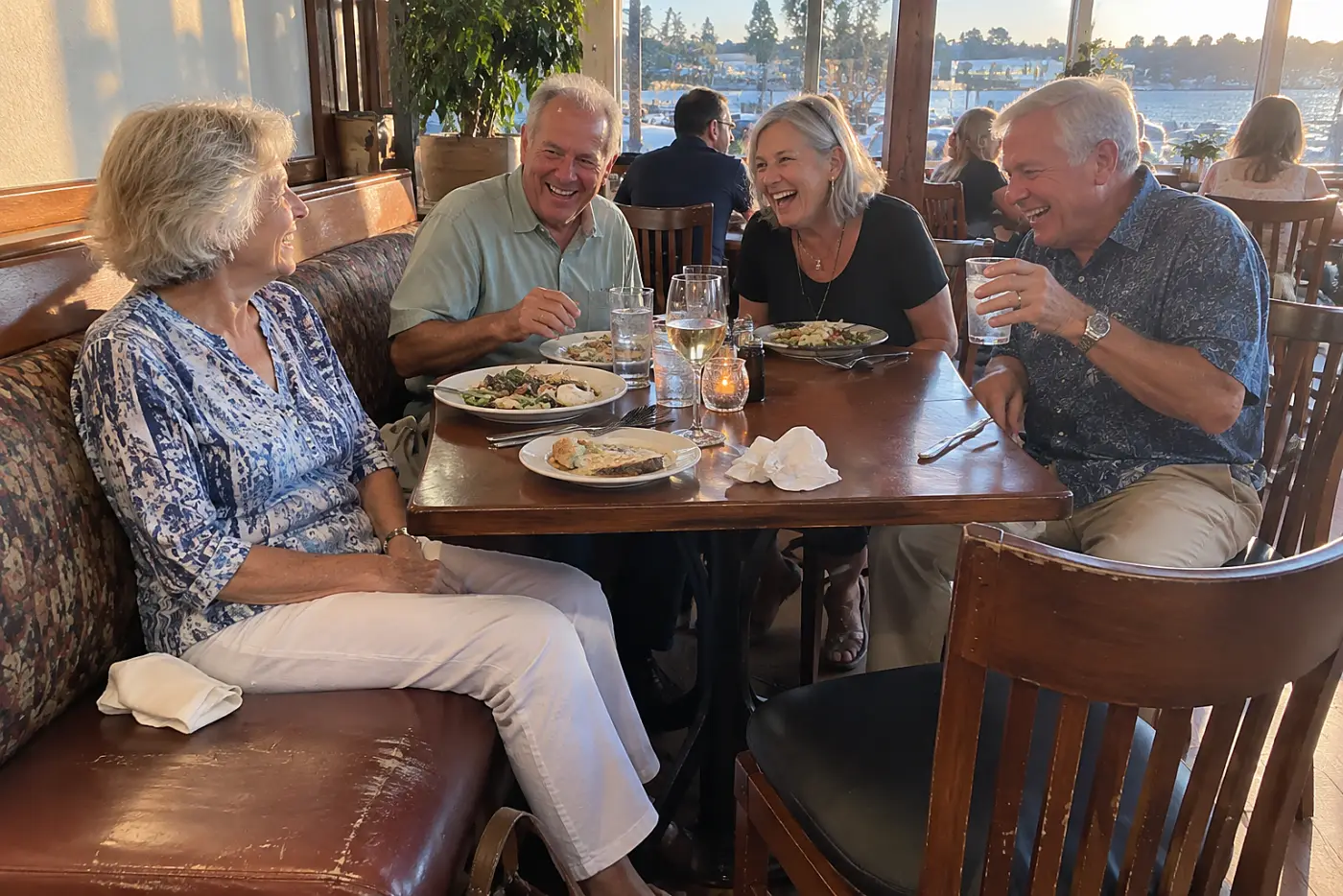 Older woman watching friends laugh around a crowded dinner table in a restaurant.