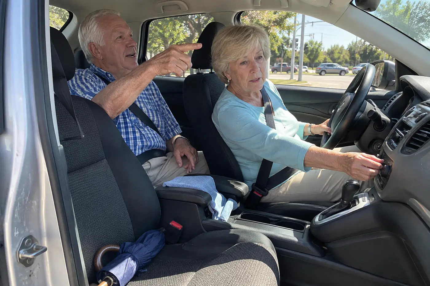 Older woman turning down the car fan while her passenger points toward an intersection.