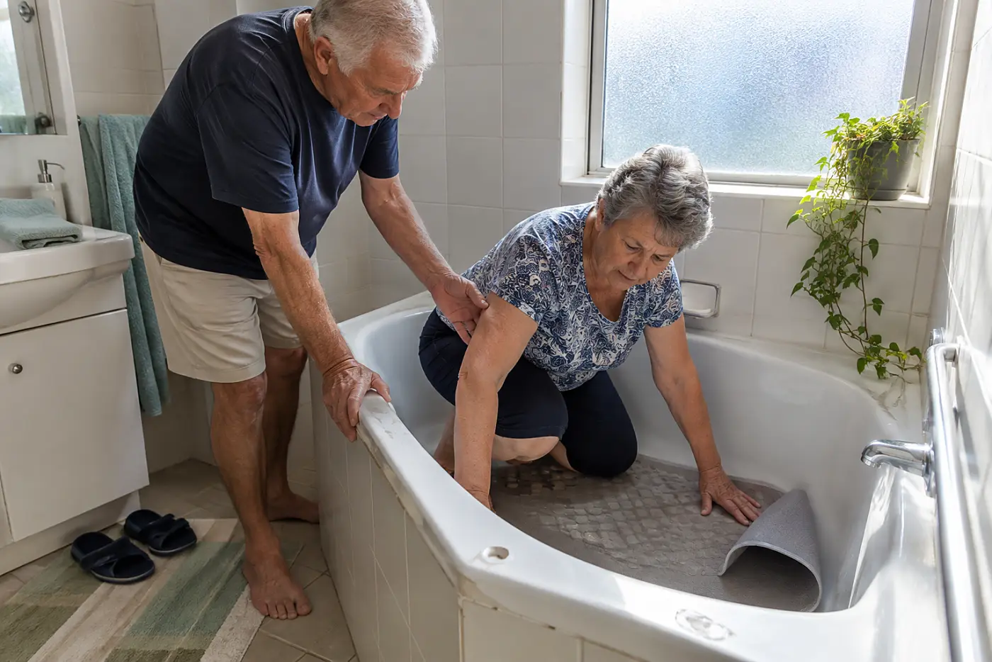 Older woman pressing a bath mat against the floor of a hotel tub.