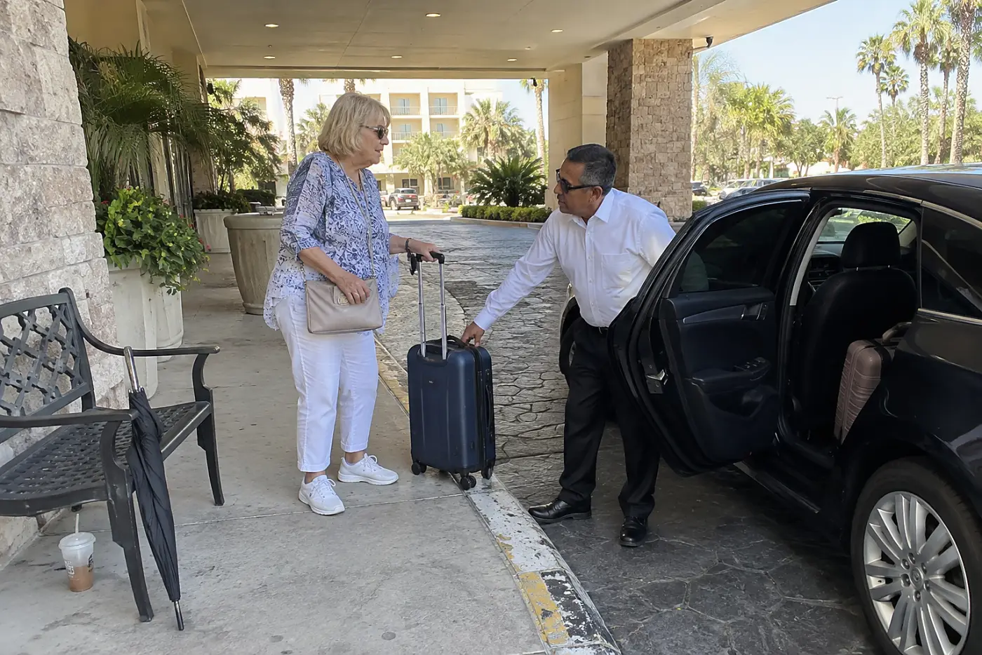 Older woman speaking with a taxi driver beneath a hotel's covered entrance.
