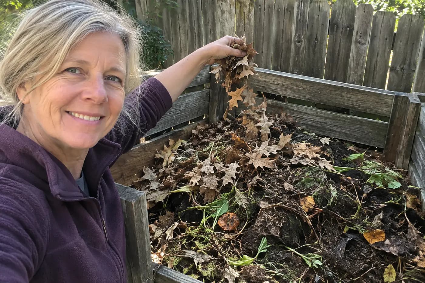 A compost heap with layers shows leaves and scraps in a backyard corner, with a woman over 50 adding dry leaves and no visible writing.