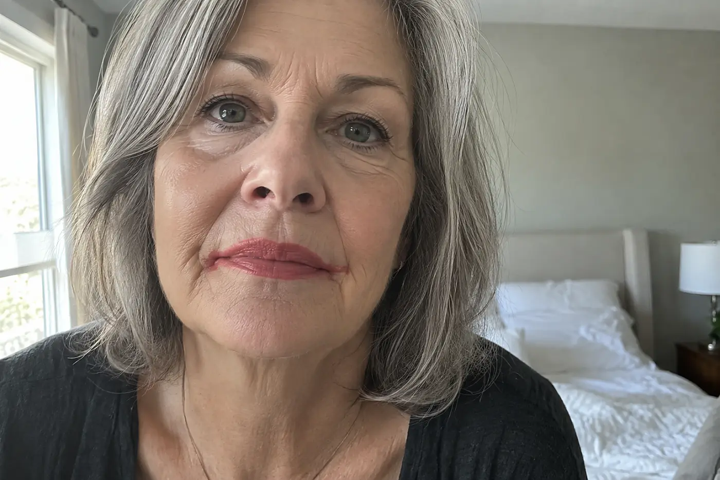 Lipstick past the lip line at both corners is centered on a woman in her sixties looking into her bedroom mirror, with no writing visible.