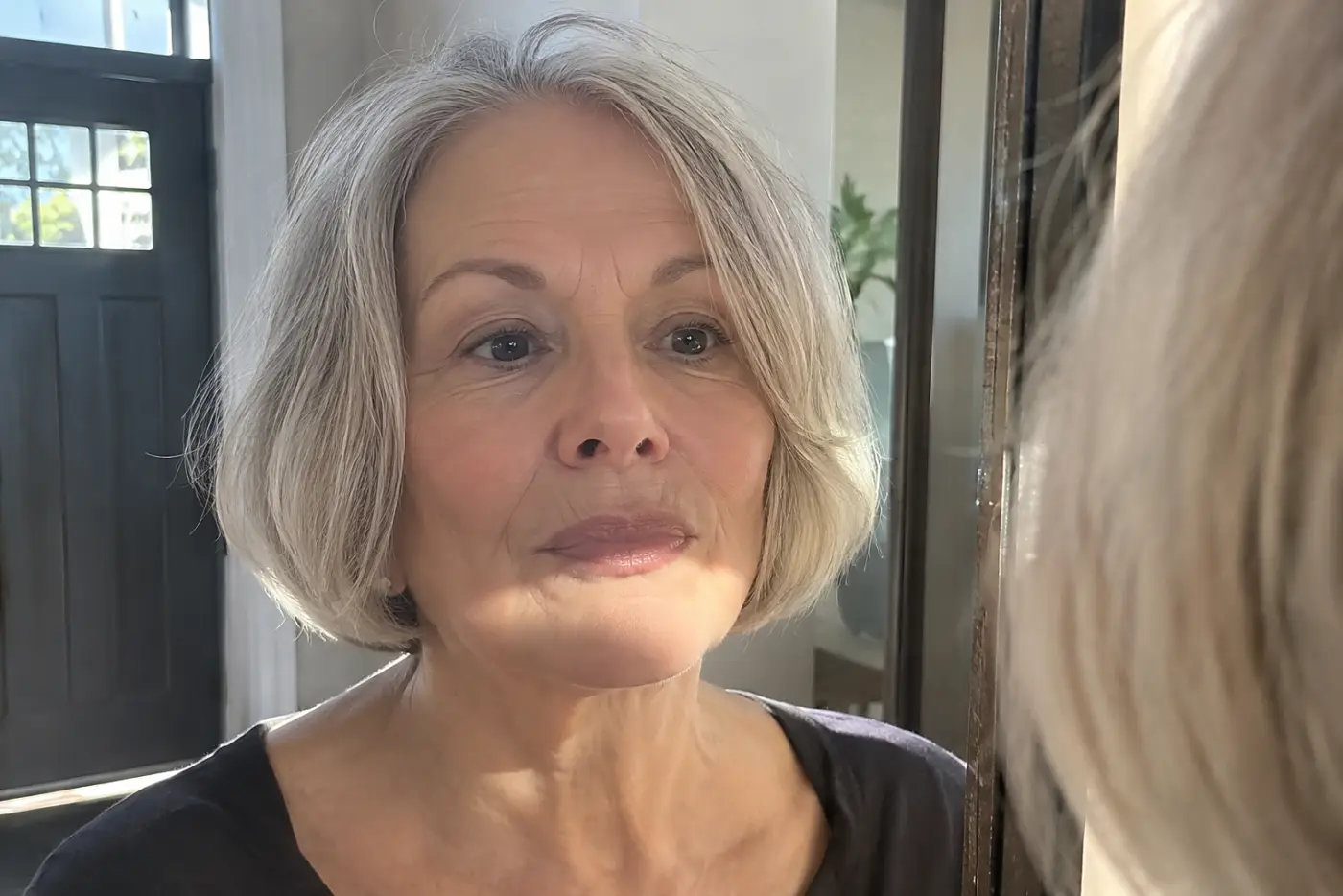 Beige lipstick is centered on a woman in her sixties looking into a mirror near her front door, with no writing visible.