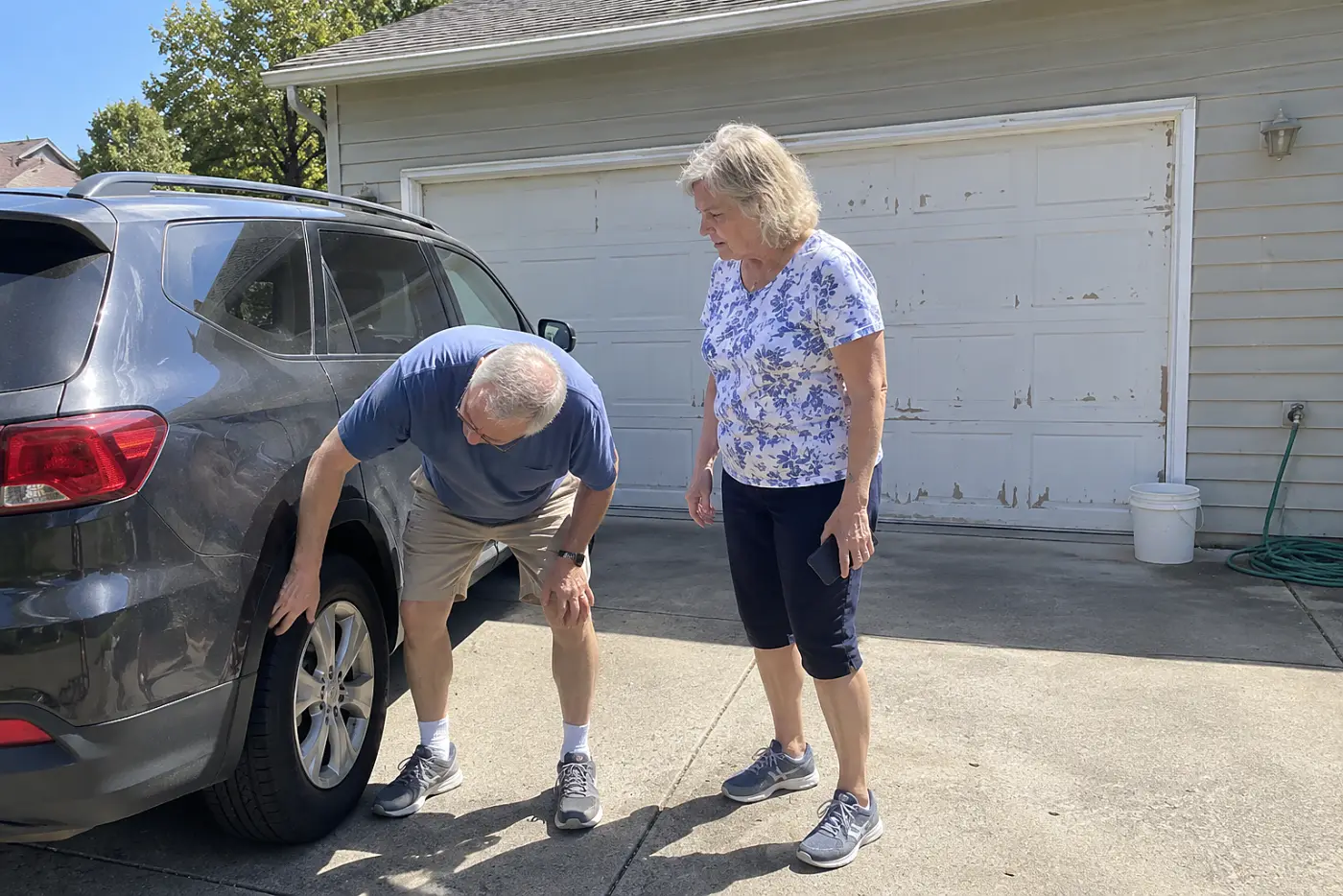 Couple talking beside a parked car after their adult child calls about a repair.