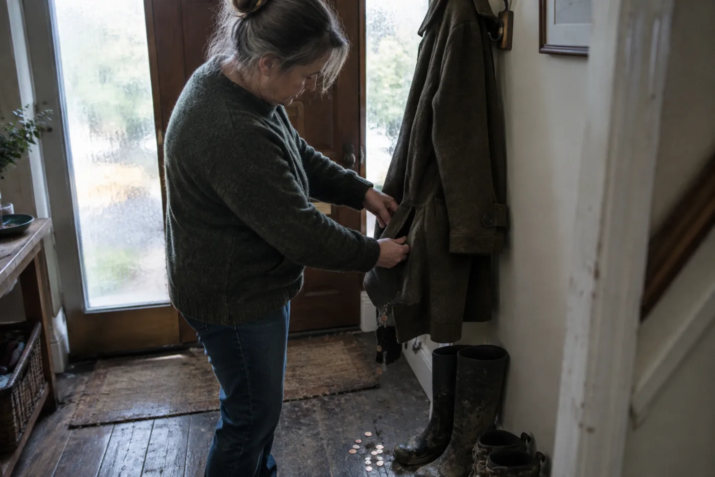 Woman patting coat pockets as coins spill onto entryway floor