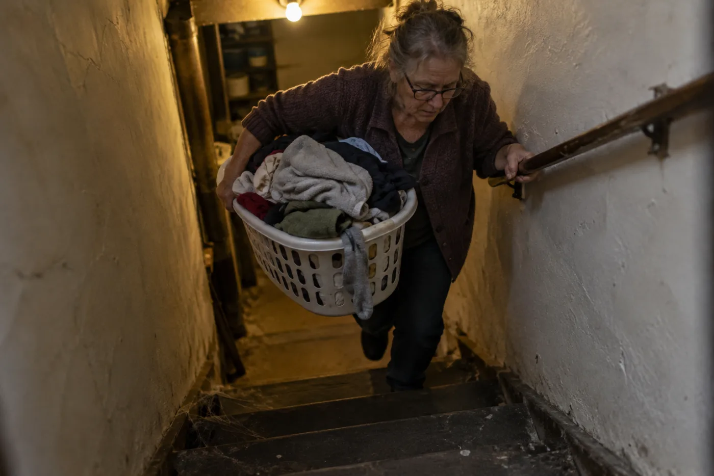 Woman climbing steep basement stairs with an overflowing laundry basket