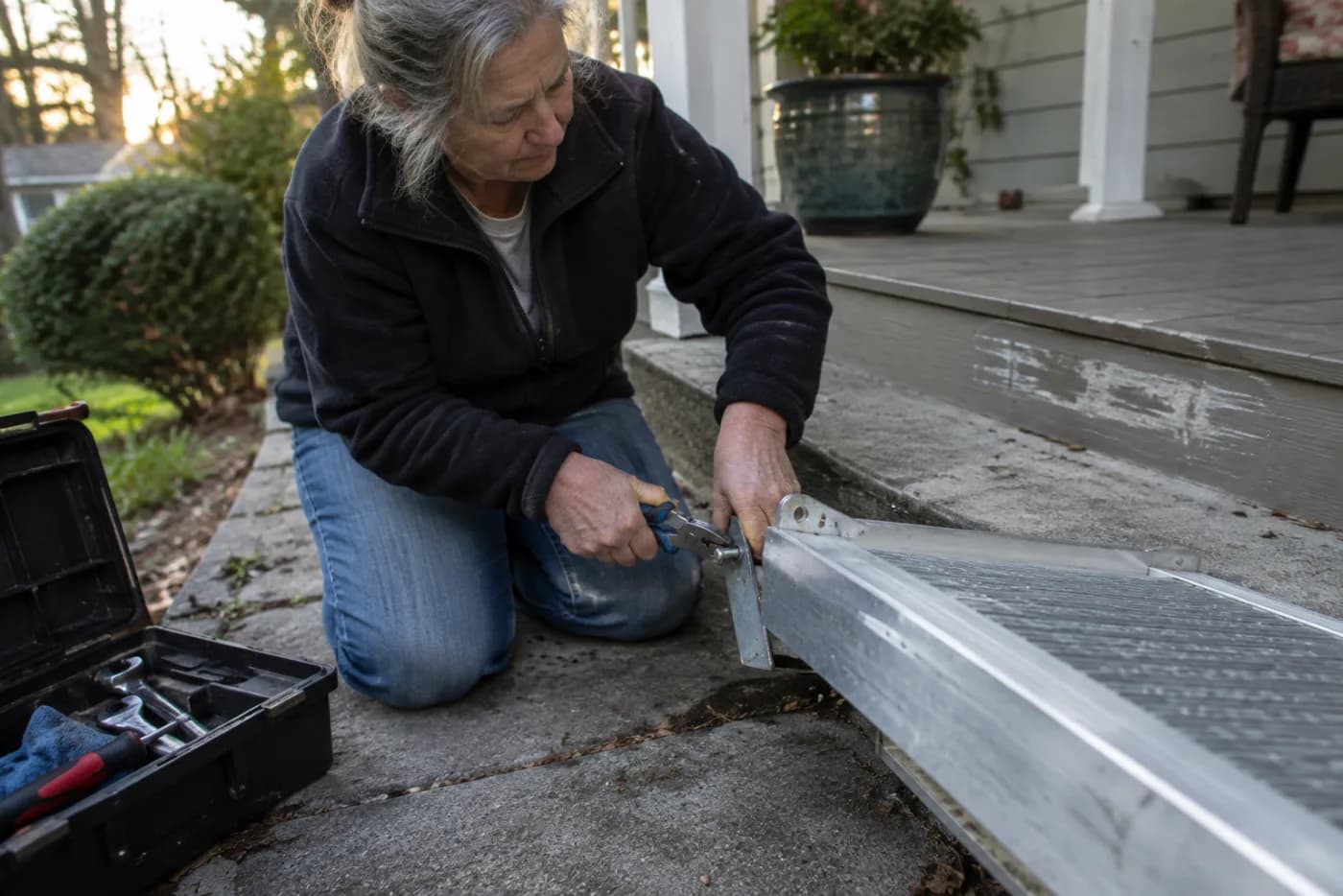 Woman unbolting a lightweight aluminum ramp from porch steps with pliers