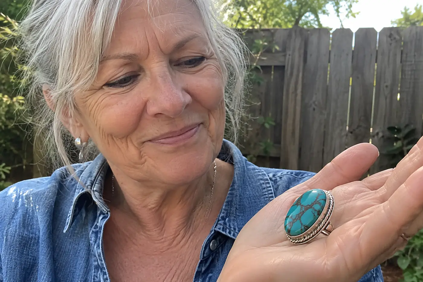 A turquoise ring with dark veins sits in the center of a woman's hand outdoors, its silver setting clear in daylight.