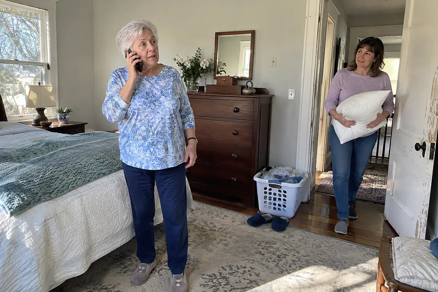 Older woman making a phone call in a spare bedroom while her daughter stands in the hall.
