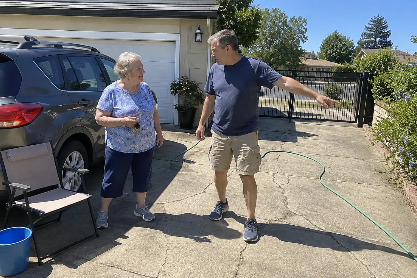 Older woman holding her car keys while discussing plans with her adult son in the driveway.
