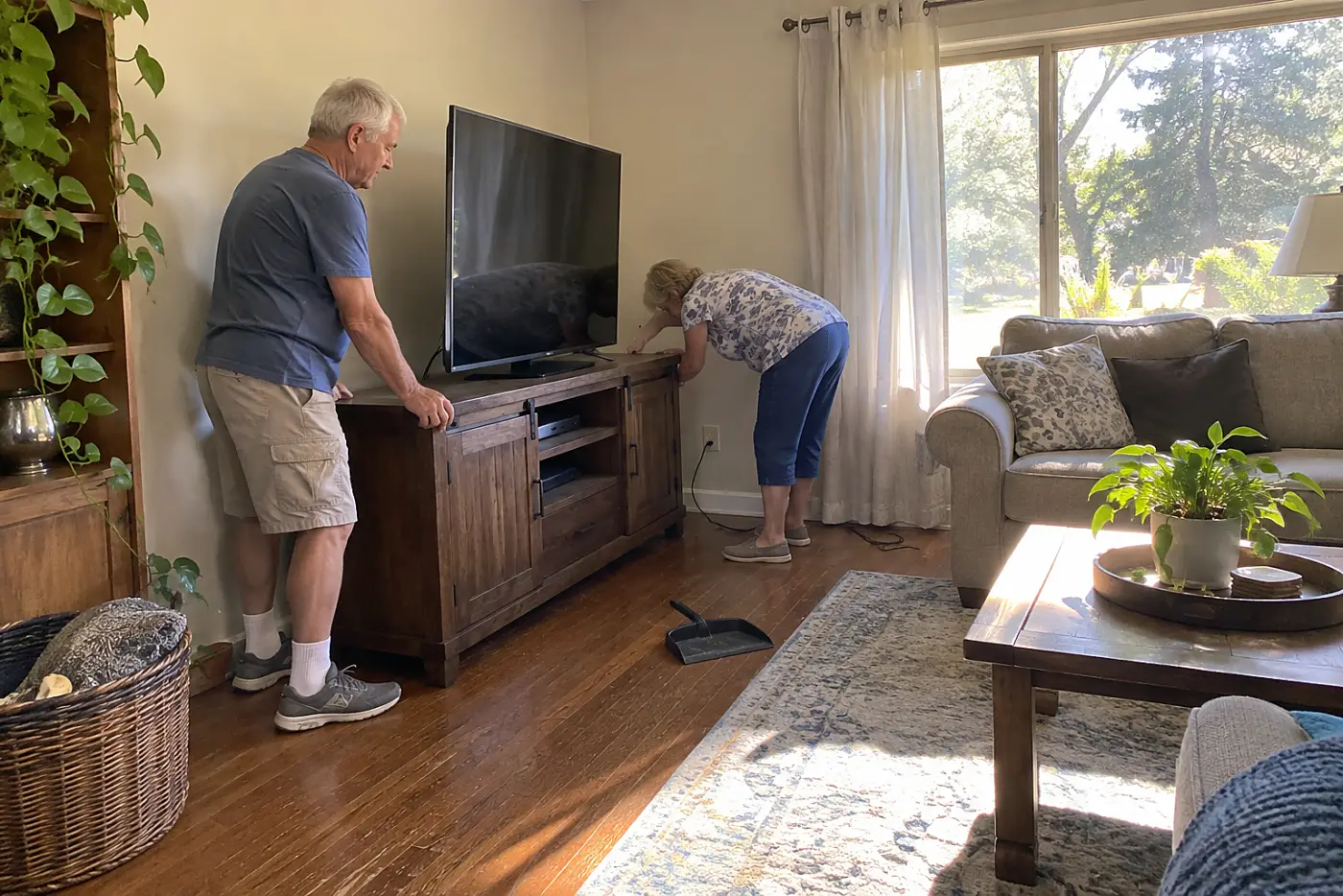 Woman checking an outlet behind a television cabinet in a living room.