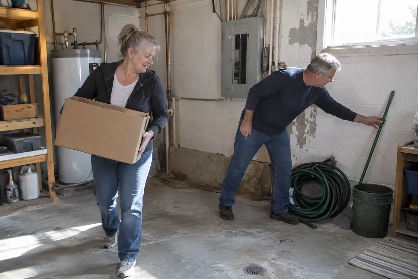 Woman moving a box away from an electrical panel in a utility room.