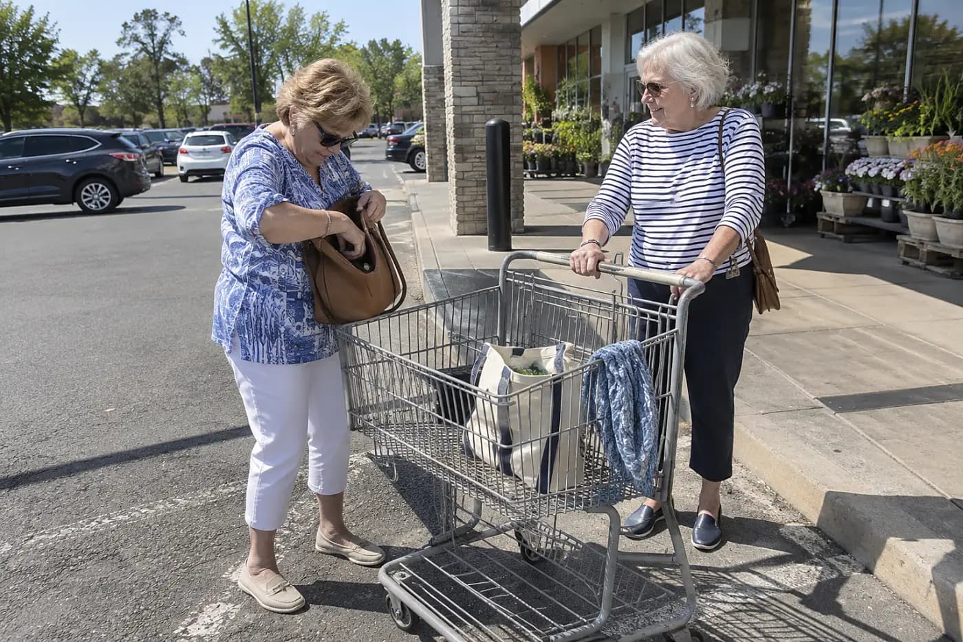 Older woman reaching into her handbag beside a grocery cart.
